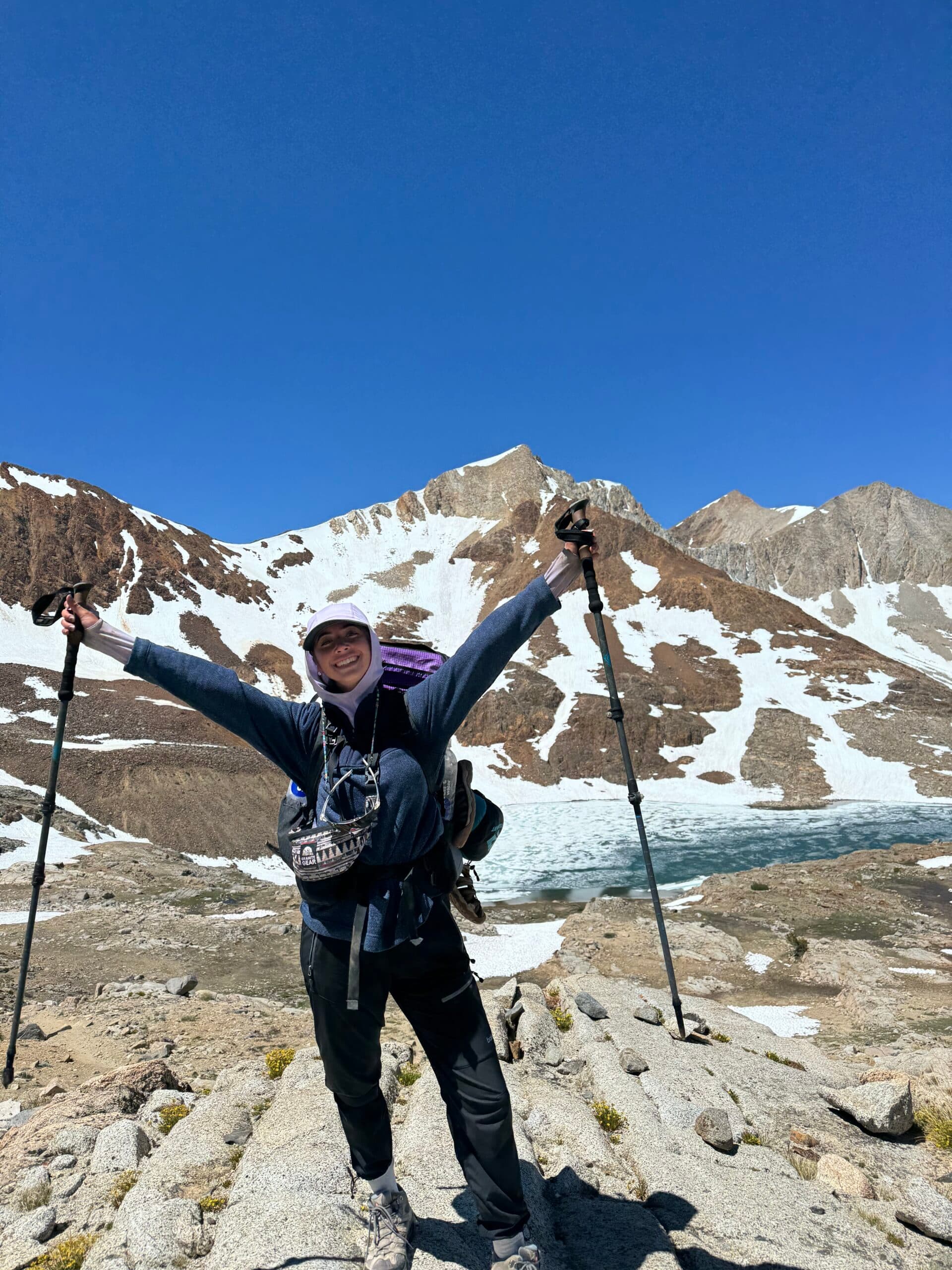 Backpacker celebrating with trekking poles raised at an alpine lake